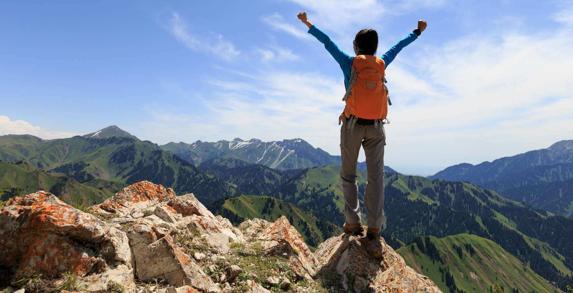 successful Hiker outstretched arms stand at cliff edge on mountain top